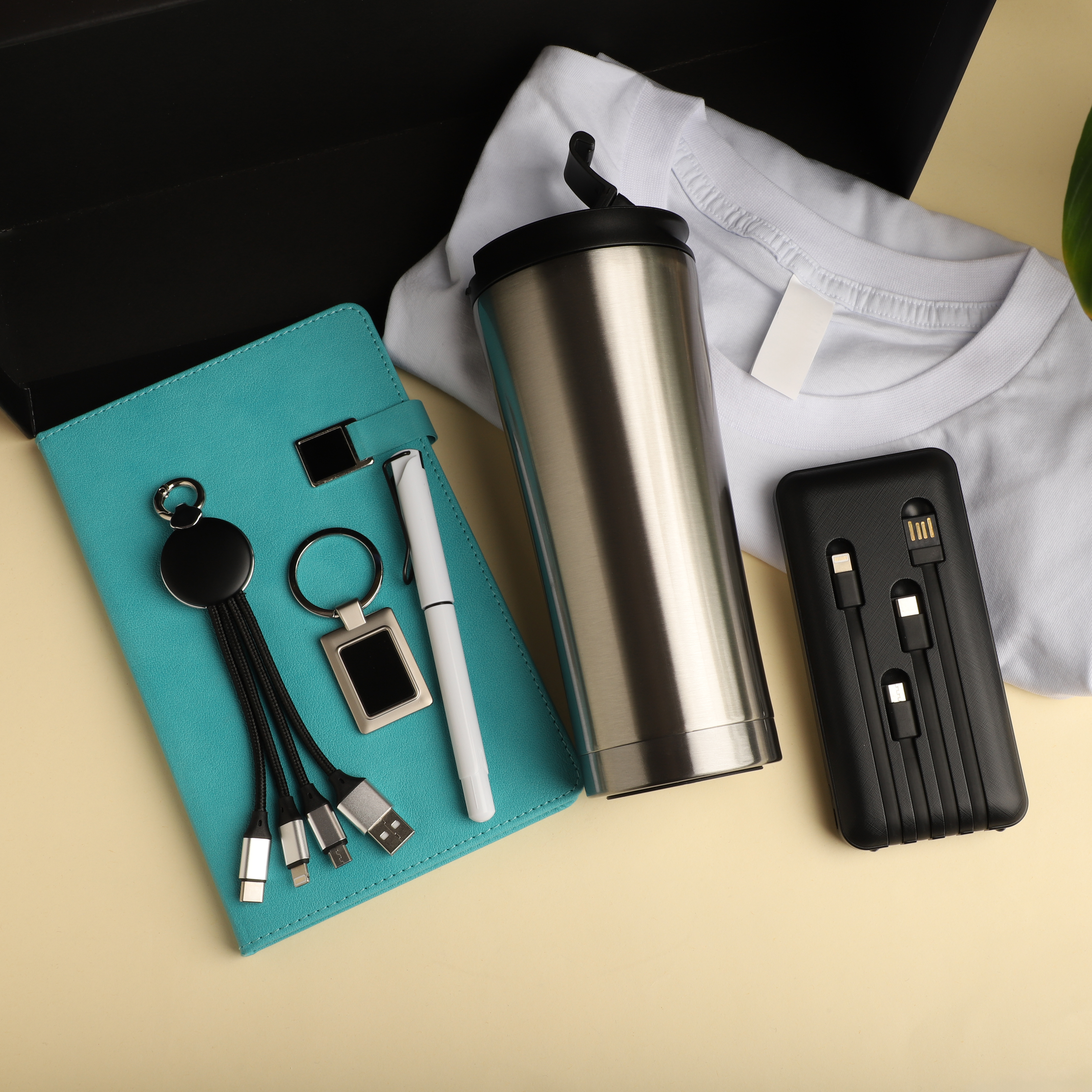 Assorted promotional items — tumbler, notebook, keychains, pen, charging cables, and t-shirt