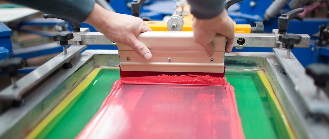 Screen printing squeegee pulling red ink across a mesh screen